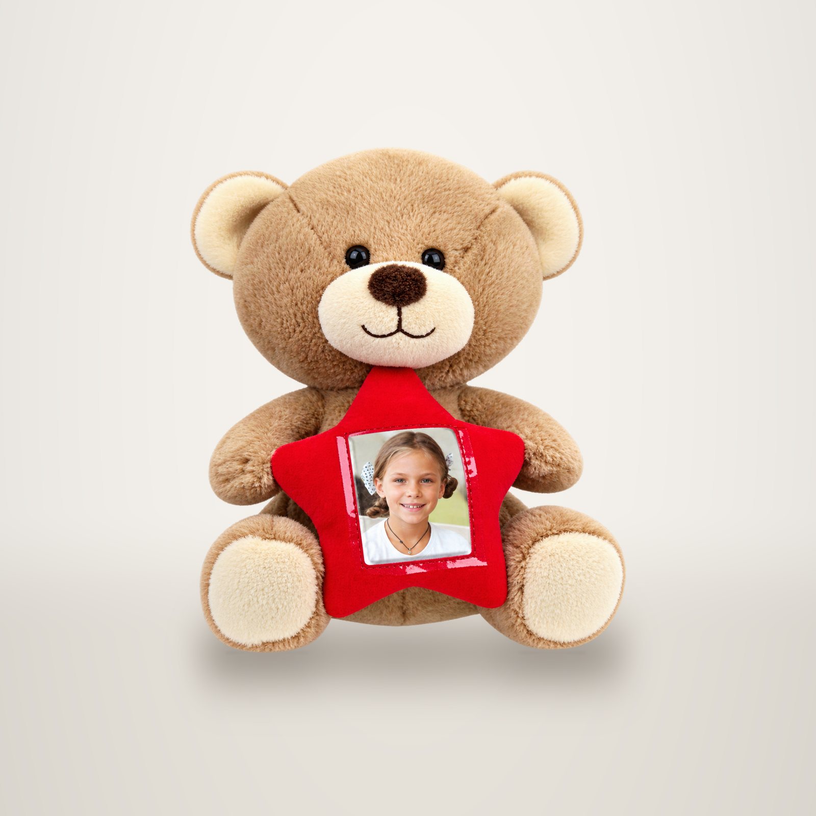 Un ours en peluche beige tient une étoile rouge contenant la photo d'une petite fille souriante.