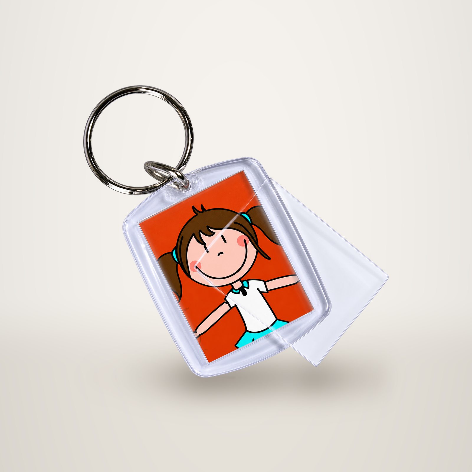 Un porte-clés en plastique transparent avec anneau métallique contient l'image dessinée d'une fillette souriante aux couettes brunes sur fond rouge, avec un film transparent qui se soulève sur le côté.
